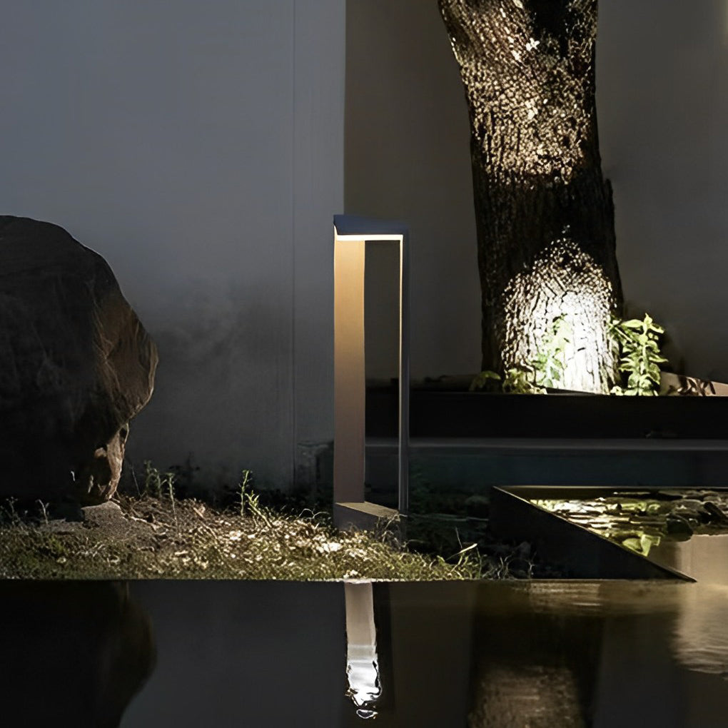 Modern architectural garden path light reflecting in a dark pool of water near a large tree ok.
