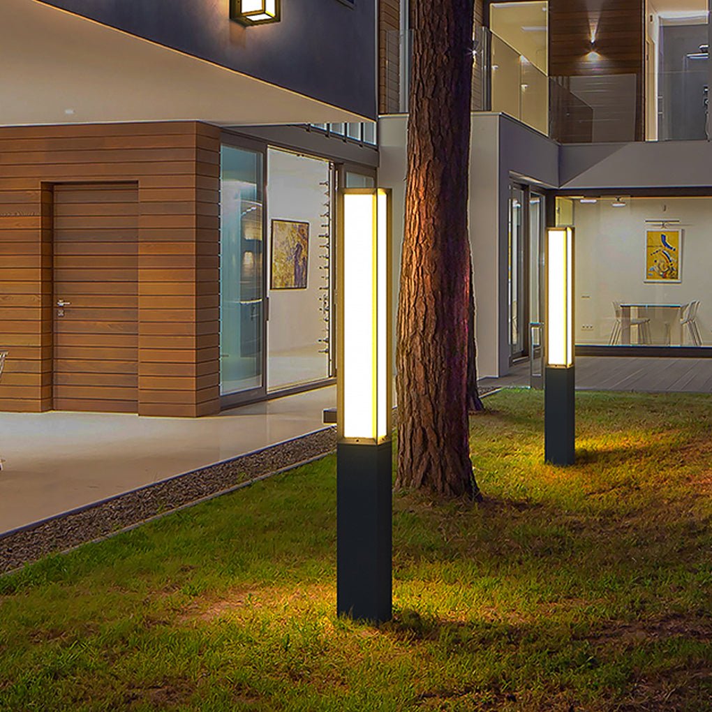 Modern black outdoor bollard lights illuminating a green grass lawn beside a wood siding home.