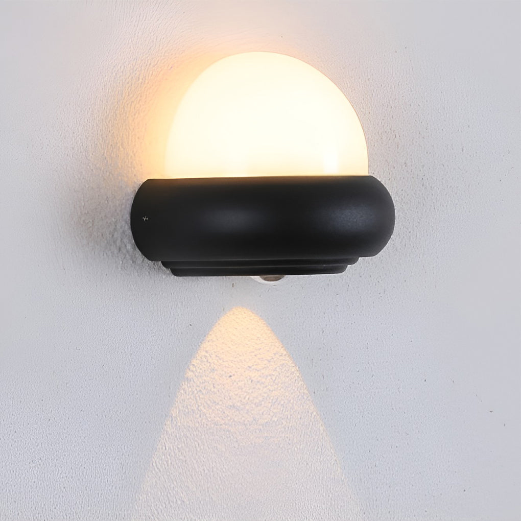 Modern globe wall sconce with black frame, casting a soft glow in a contemporary outdoor setting.