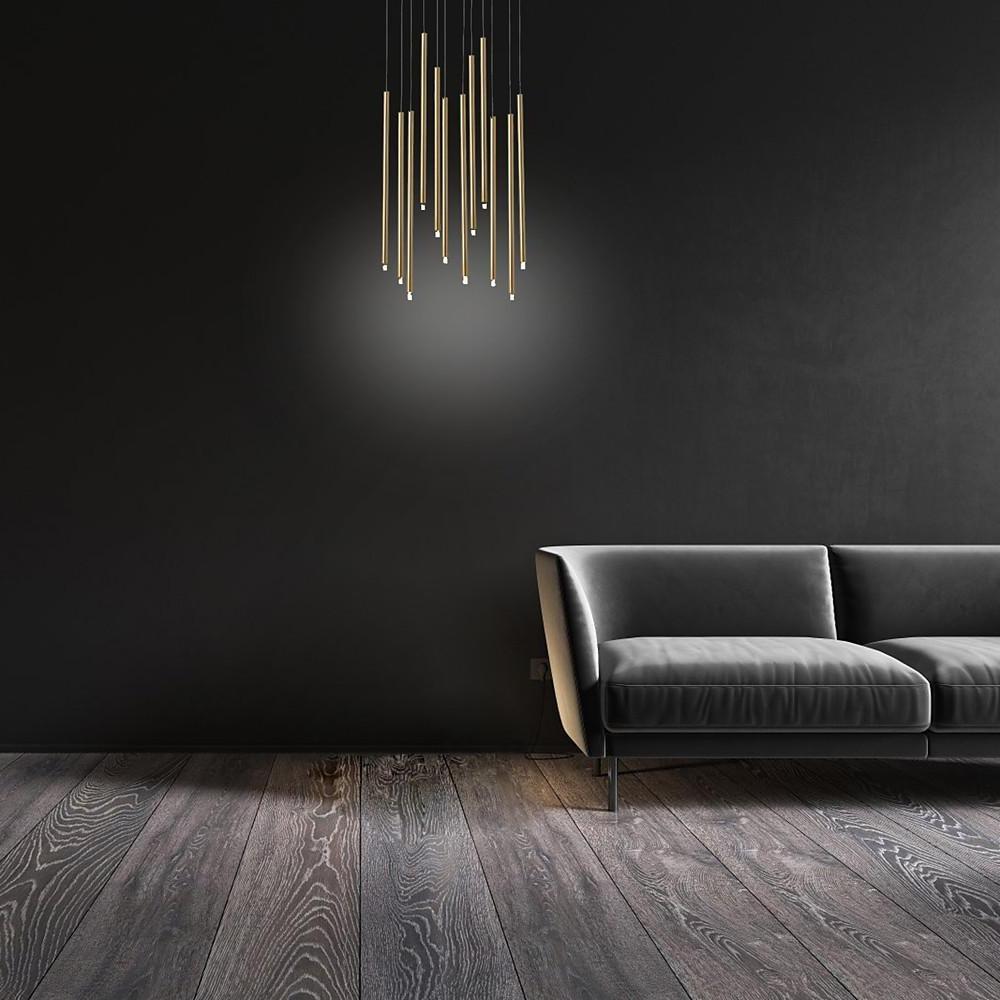 Modern gold staircase chandelier staggered heights in a moody lounge with a plush grey sofa.