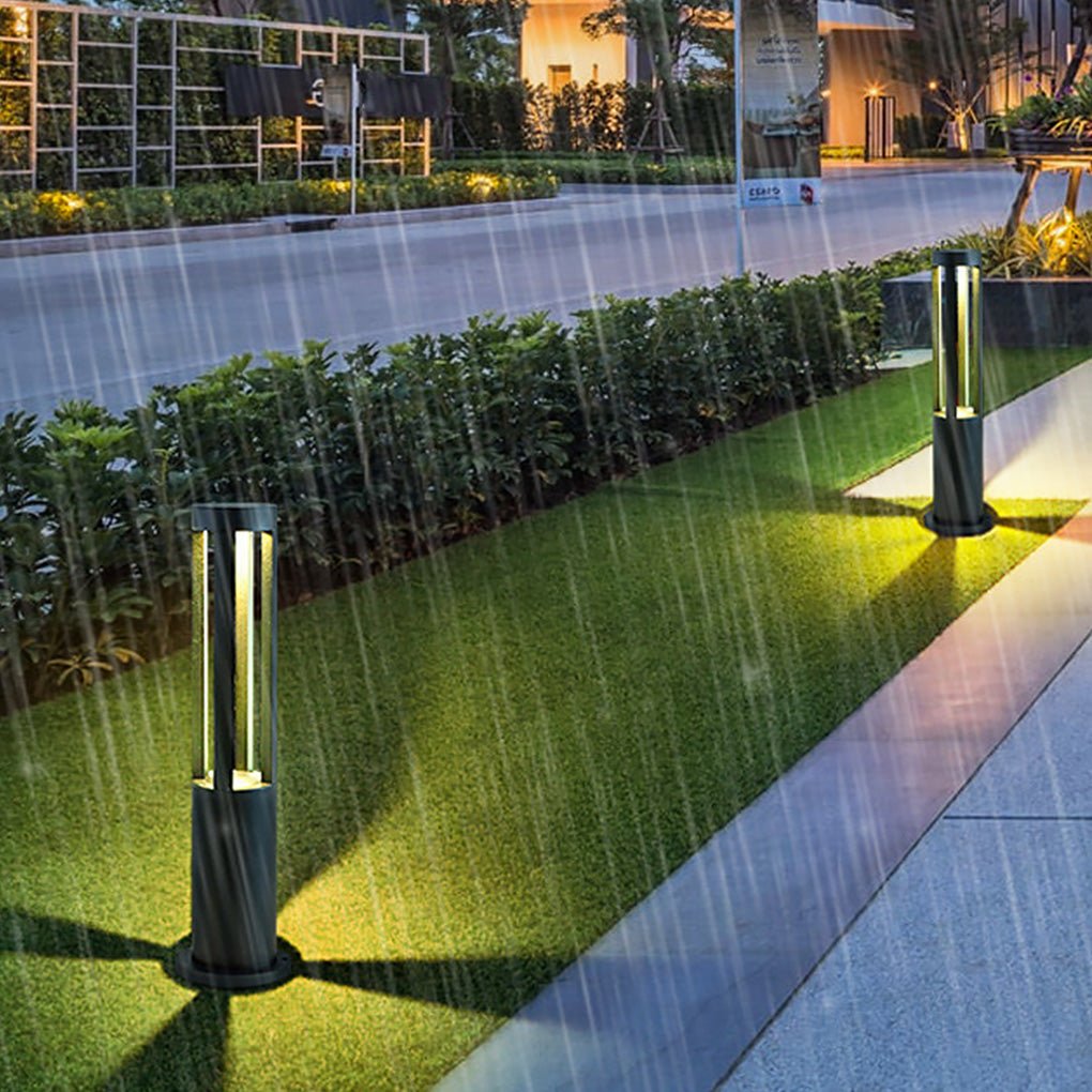 Modern outdoor bollard lights casting light on a stone pathway beside a house.