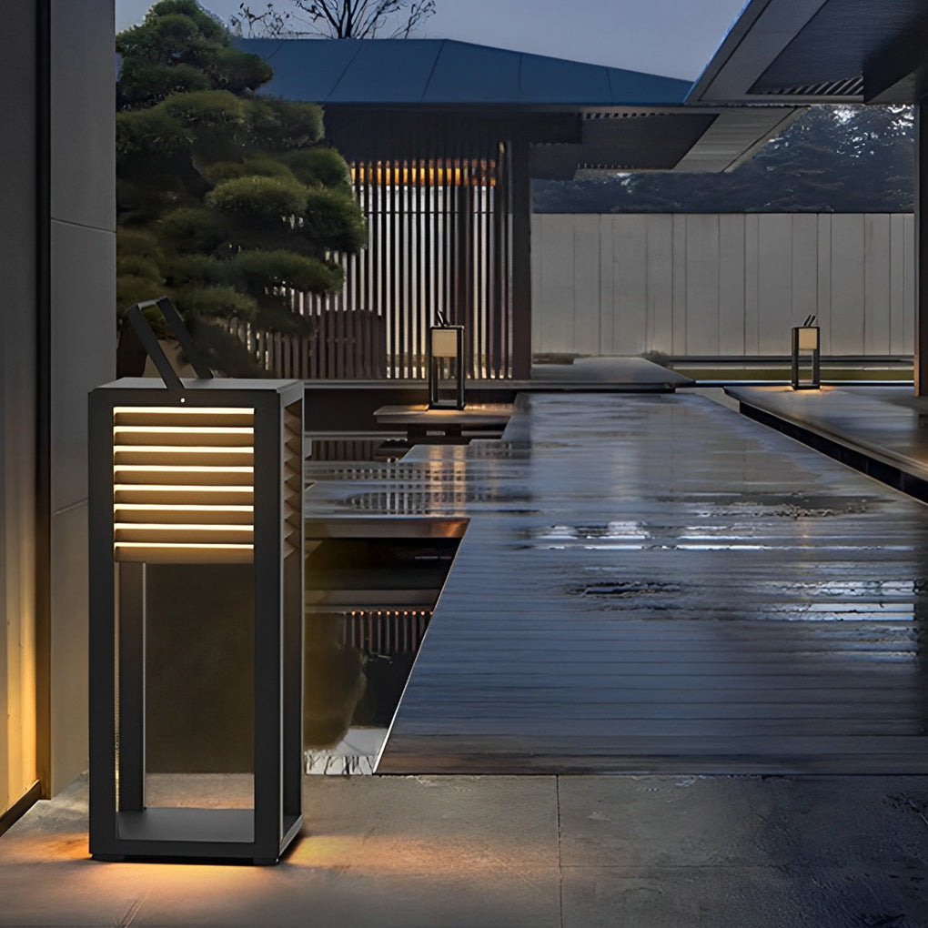 Modern outdoor floor lantern beside water feature reflecting warm light.