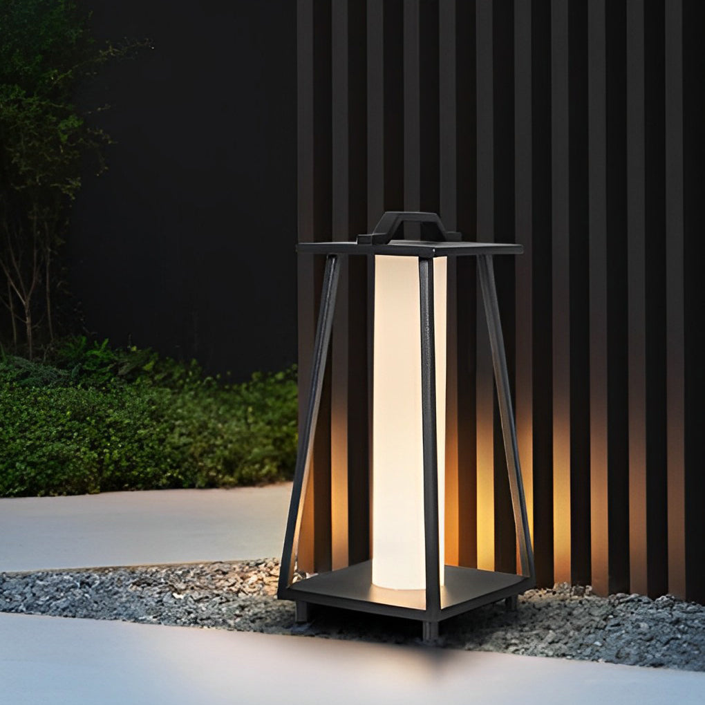 Modern portable outdoor lantern standing on gravel beside a minimalist garden wall at night.