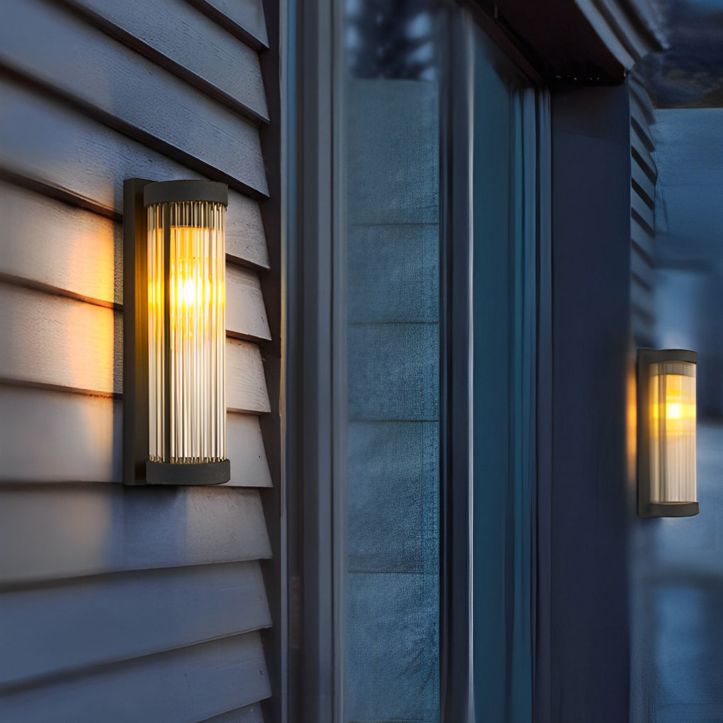 Modern vertical outdoor wall mount lights casting a warm glow on dark blue vinyl siding near a window frame.