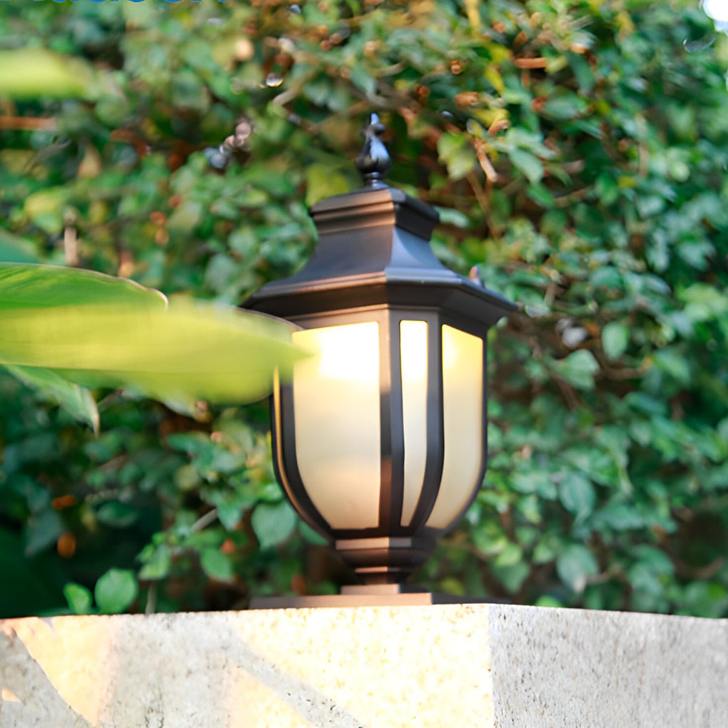 Black vintage outdoor pillar lantern with yellow glass lens mounted on a sunlit garden wall.