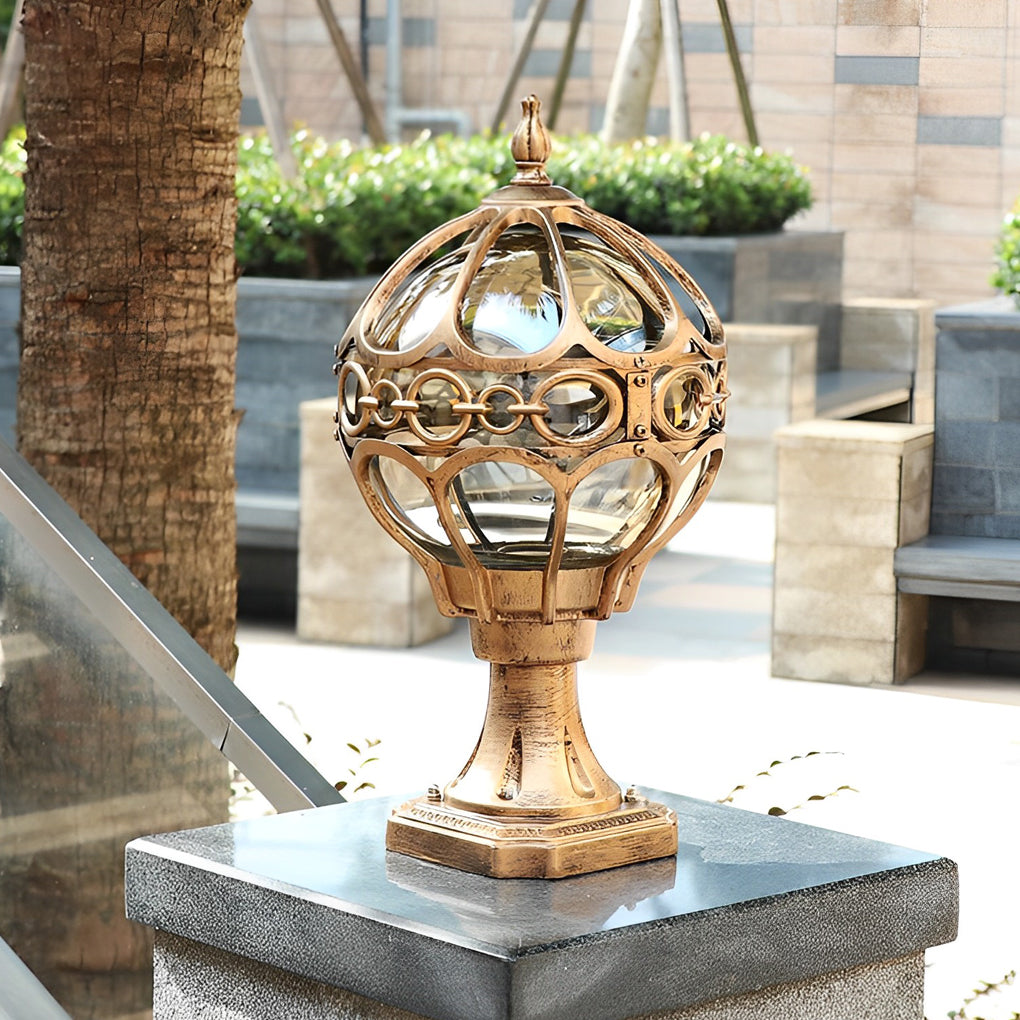 Modern outdoor globe pillar lights with a gold finish, mounted on a concrete pillar near tropical plants.