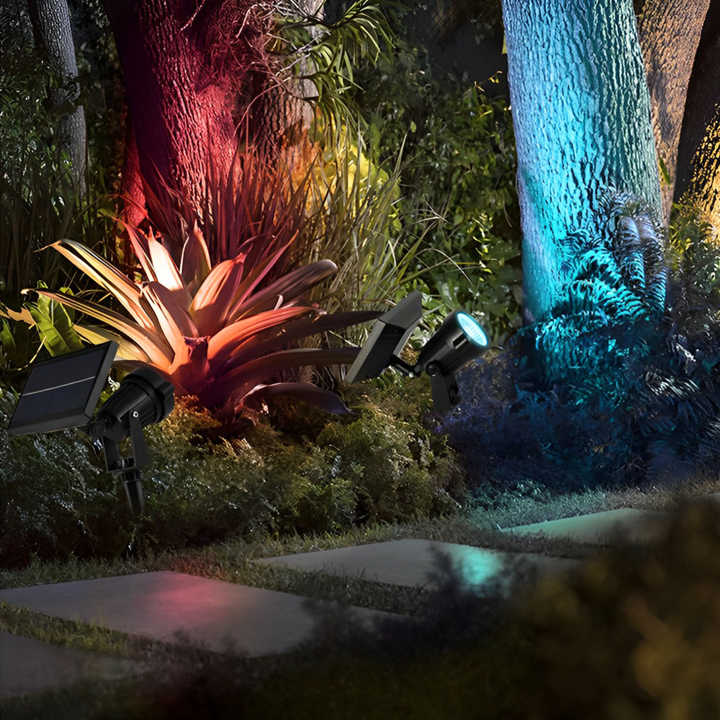 Outdoor ground spike solar lights casting colorful accent lighting on trees and plants in a landscaped night garden.