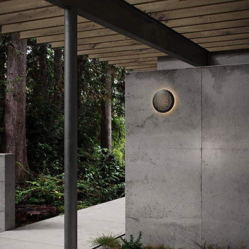 Perforated metal wall sconce installed on a concrete wall under a covered walkway.