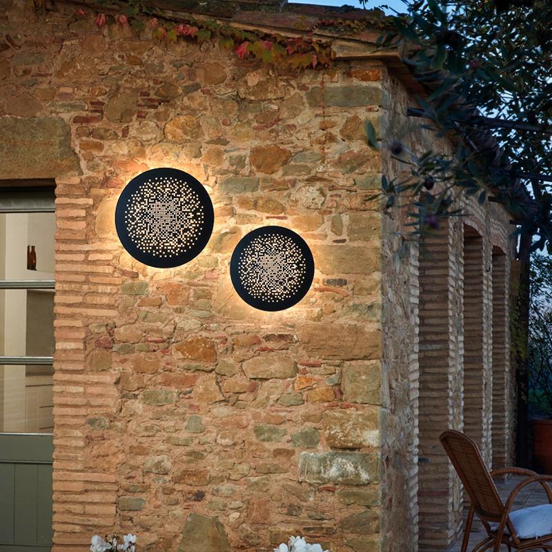 Perforated metal wall sconce pair mounted on a rustic stone exterior wall.