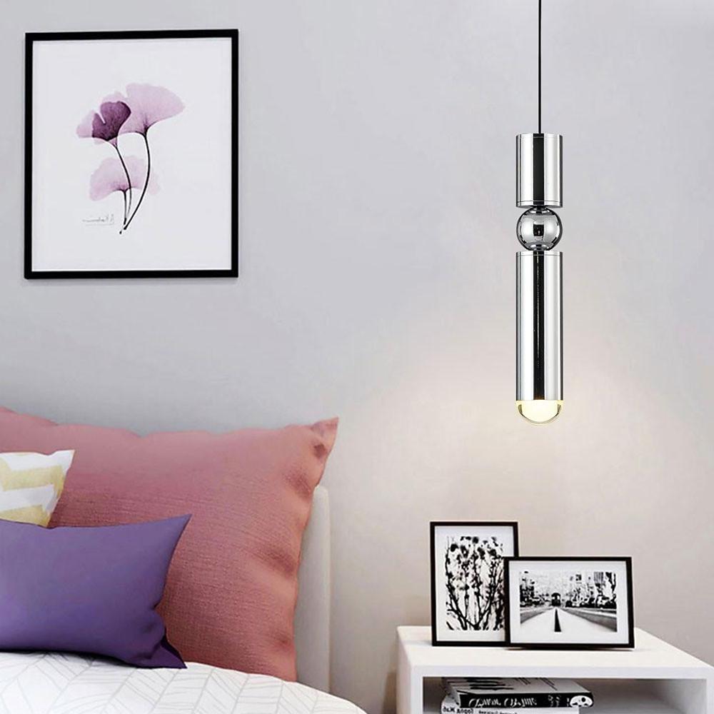Polished chrome cylinder pendant light with orb detail beside a nightstand in a white bedroom.