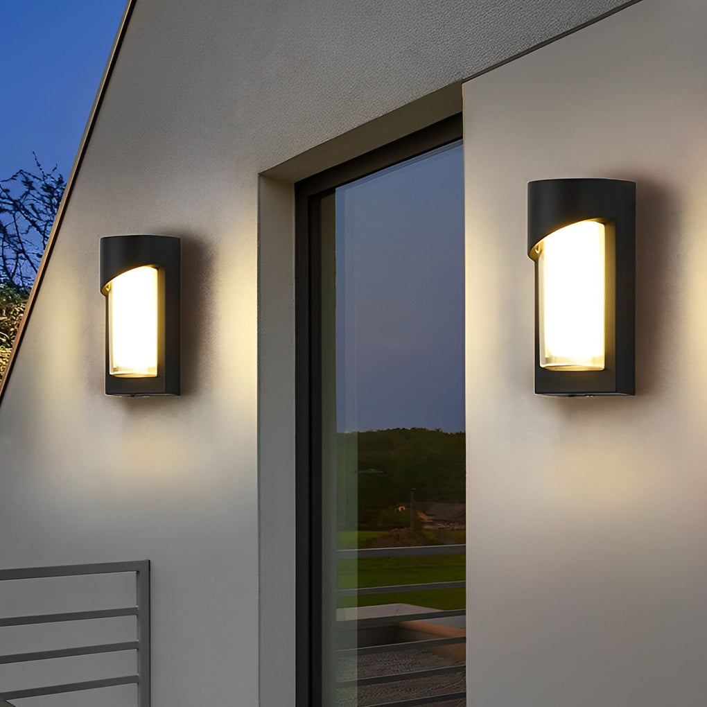 Black outdoor wall light with rectangular shape on textured wall near plants.