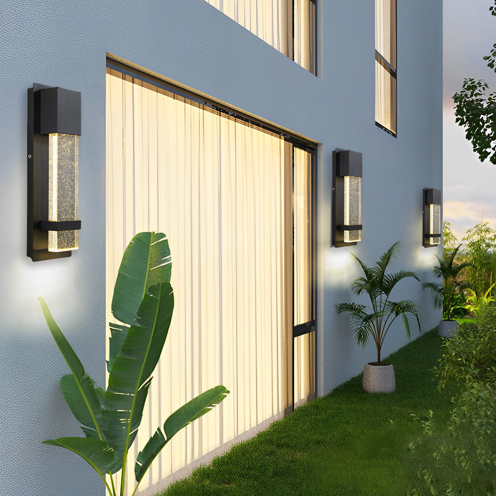 Modern rectangular outdoor wall lights mounted on exterior wall next to large windows and garden plants.