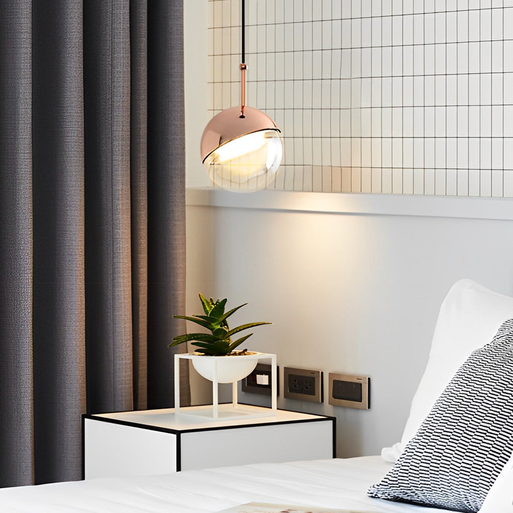 Elegant rose gold globe pendant light adding a warm glow next to a bed in a modern bedroom.