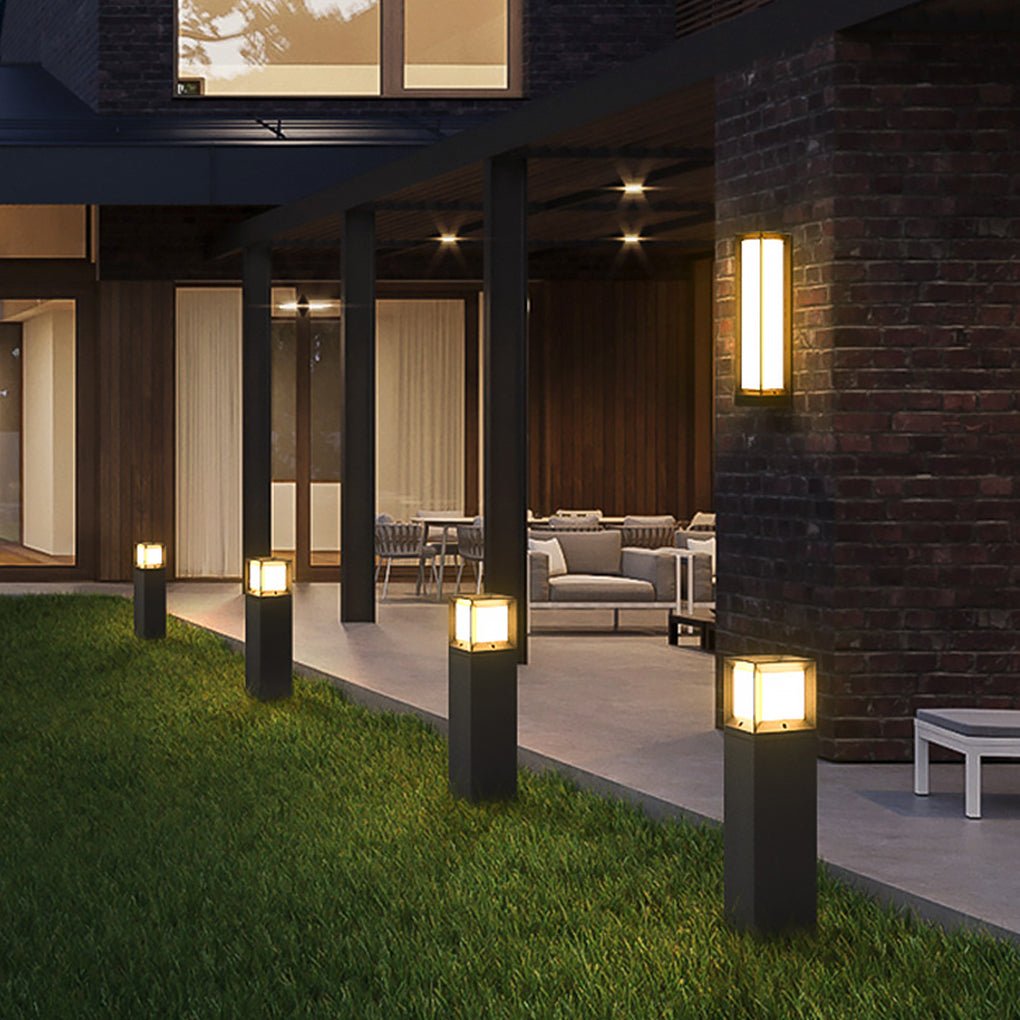 Row of square black outdoor bollard lights illuminating a green lawn near a modern patio area.