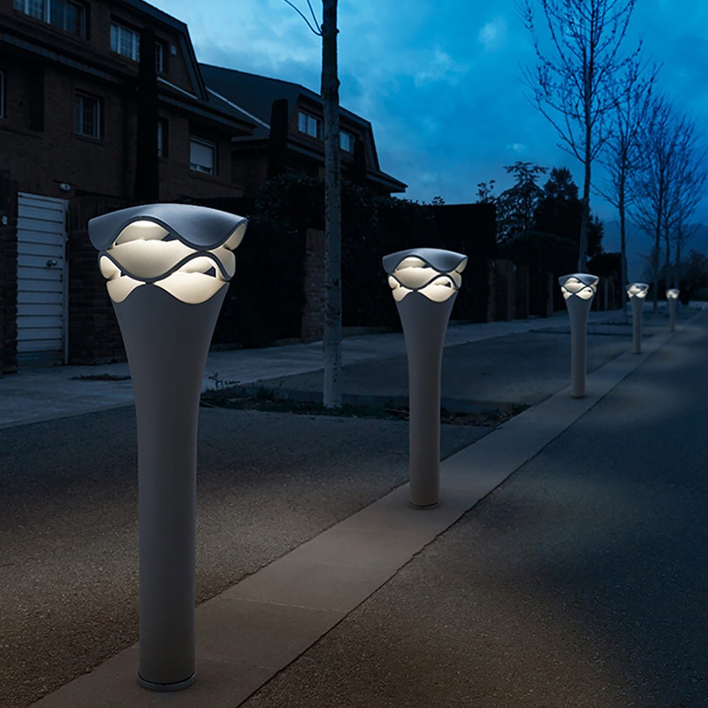 Row of tall wave design path lights lining a dark driveway and sidewalk at a luxury residence.
