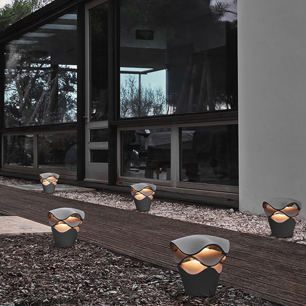 Short wave design path lights placed on dark gravel beside a modern luxury glass home exterior.