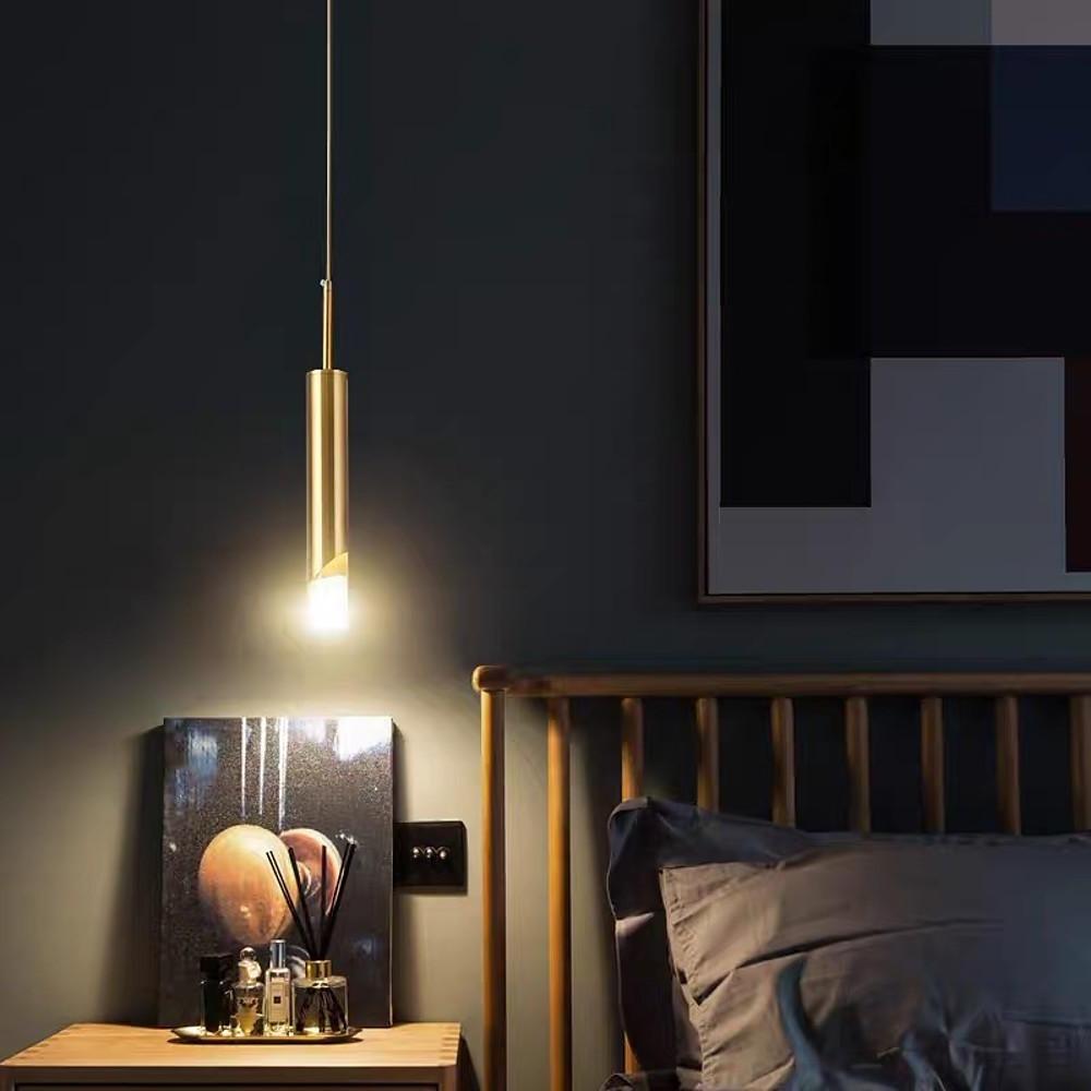 Single Slanted Gold Cylinder Pendant light as a minimalist bedside lamp on a wooden table.