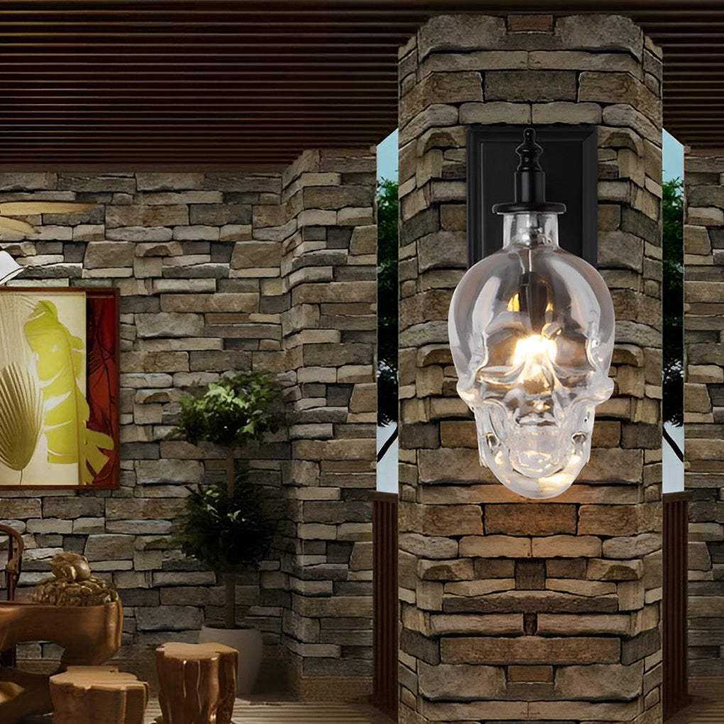 Outdoor glass lamp shades for wall lights featuring a skull design, mounted on a stone pillar near a garden area.