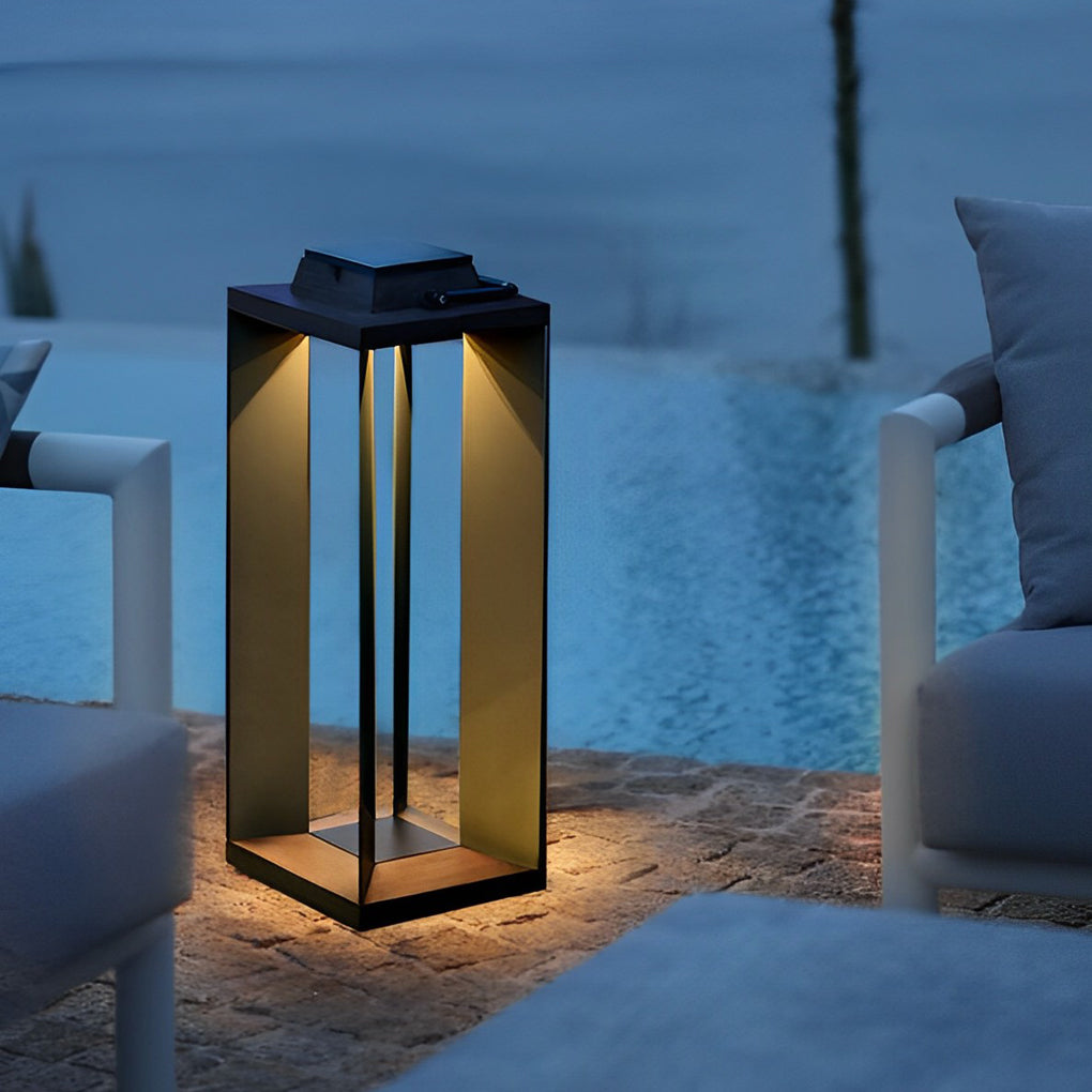 Tall portable solar lantern providing accent lighting next to an outdoor sofa at night.