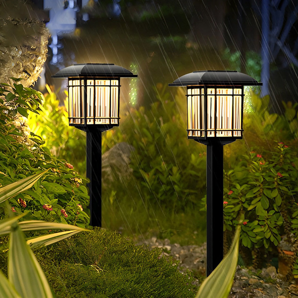 Solar outdoor lawn light with a black finish, glowing warmly in a lush garden setting.