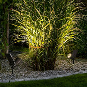 Solar powered spotlights used to highlight tall ornamental grass in a garden bed, providing focused outdoor accent lighting.
