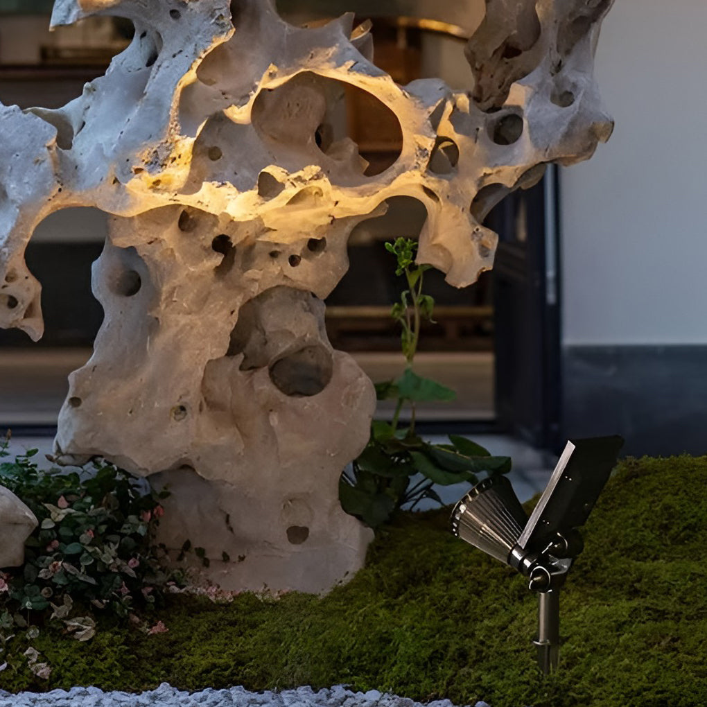 Solar powered spotlights illuminating decorative stone sculpture in a landscaped outdoor setting at night.