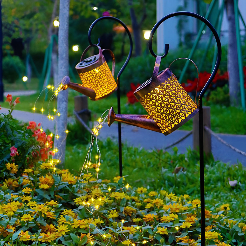 Solar watering can lights displayed above a colorful flower bed with cascading LED string lights.