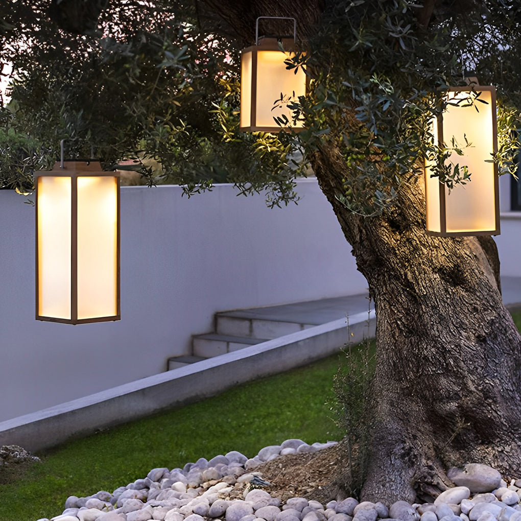 Square handheld lantern illuminating garden pathway with decorative pebbles.