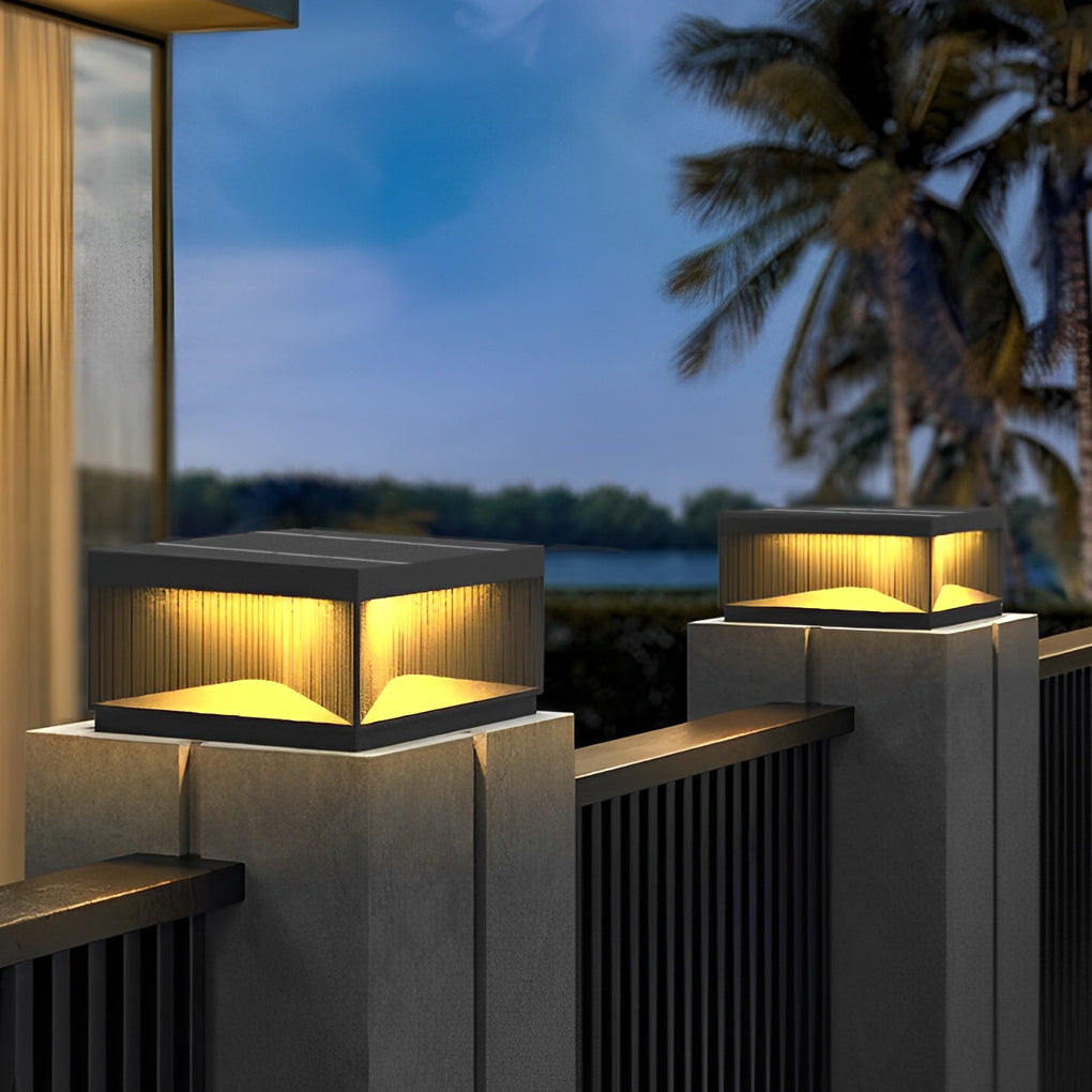 Square outdoor pillar lights placed on fence posts beside terrace with palm trees at dusk.