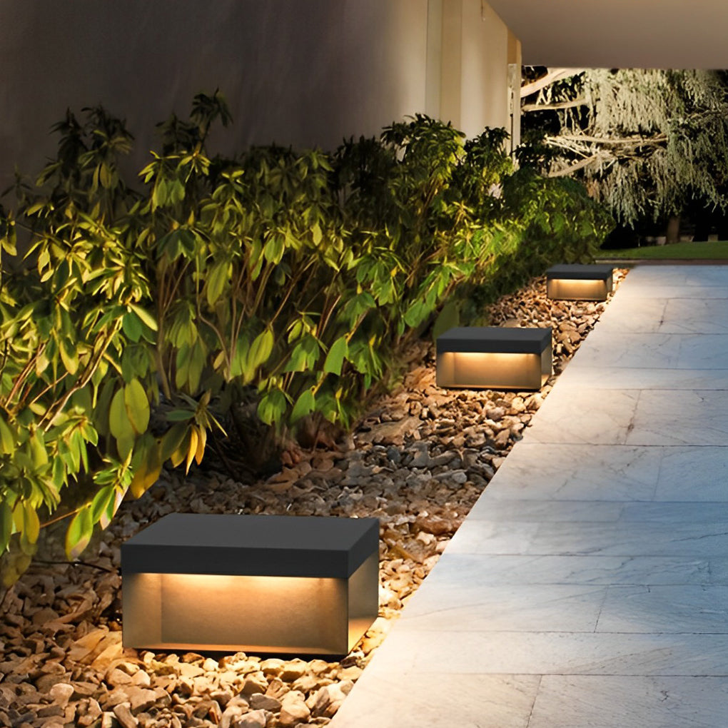 Square solar deck lights installed beside garden walkway highlighting landscaping at night.