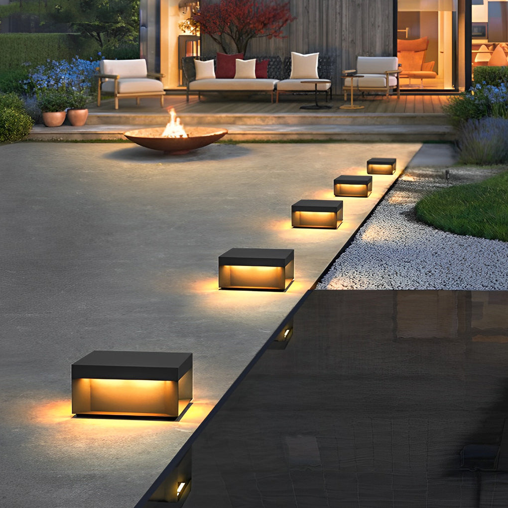 Square solar deck lights arranged along outdoor pathway edge creating warm and even ground lighting.