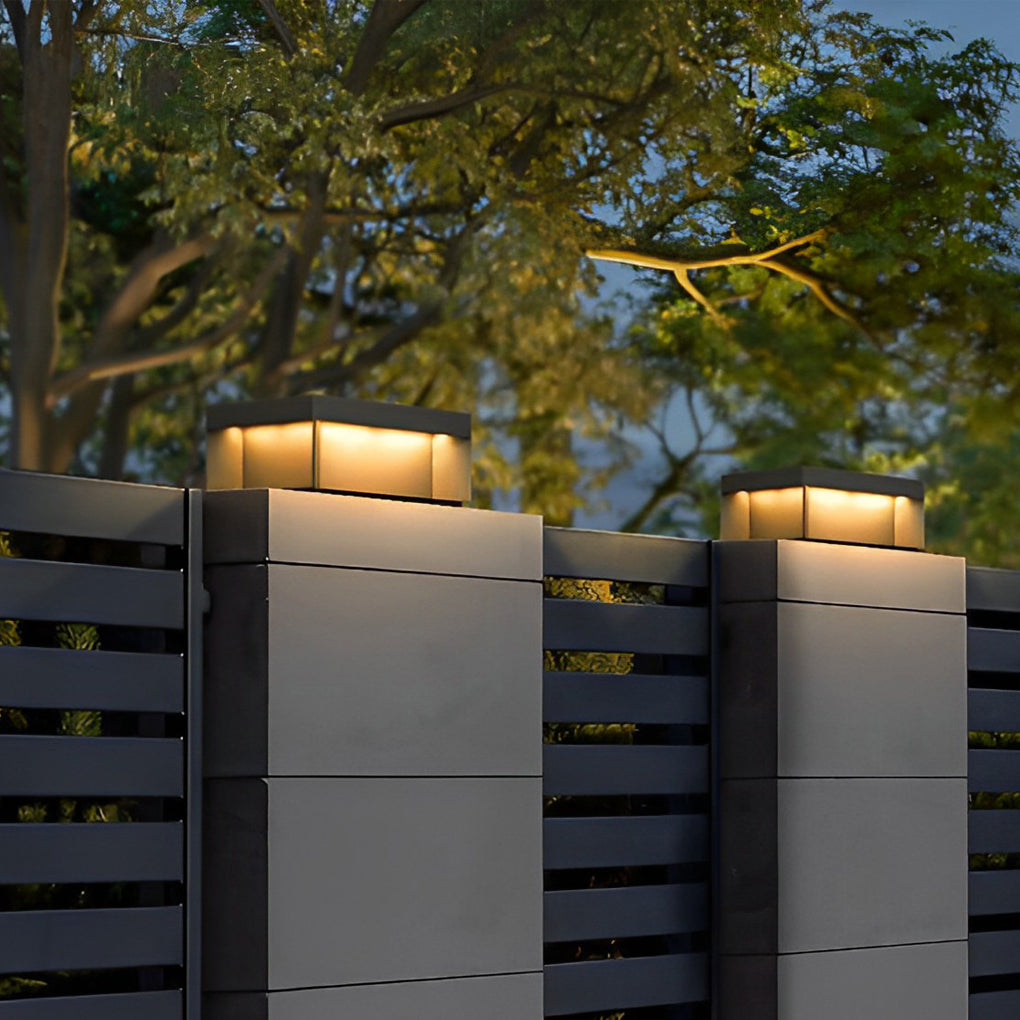 Square solar deck lights installed on outdoor railing posts with trees in background at dusk.