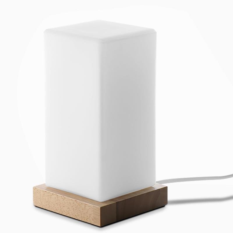 Square table light glowing softly with frosted shade and wooden base.