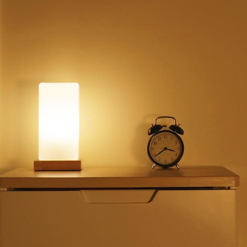 Square table light on a floating shelf casting soft light beside a classic alarm clock.