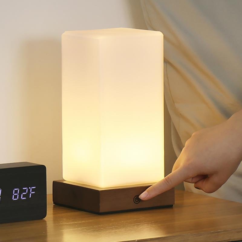 Square table light with touch control being operated by hand on a bedside table.