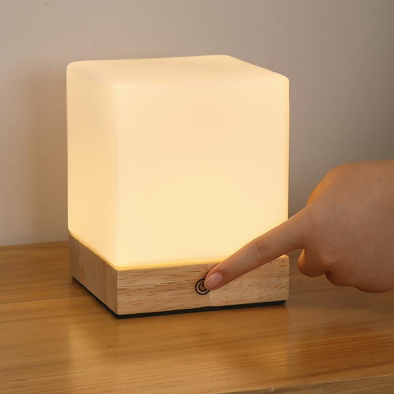 Square wood lamp with a warm light, placed on a white surface.