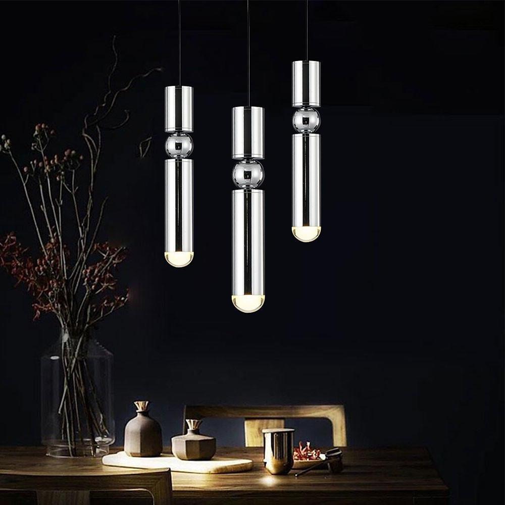 A staggered trio of chrome cylinder pendant lights with sphere detail over a dark dining table.