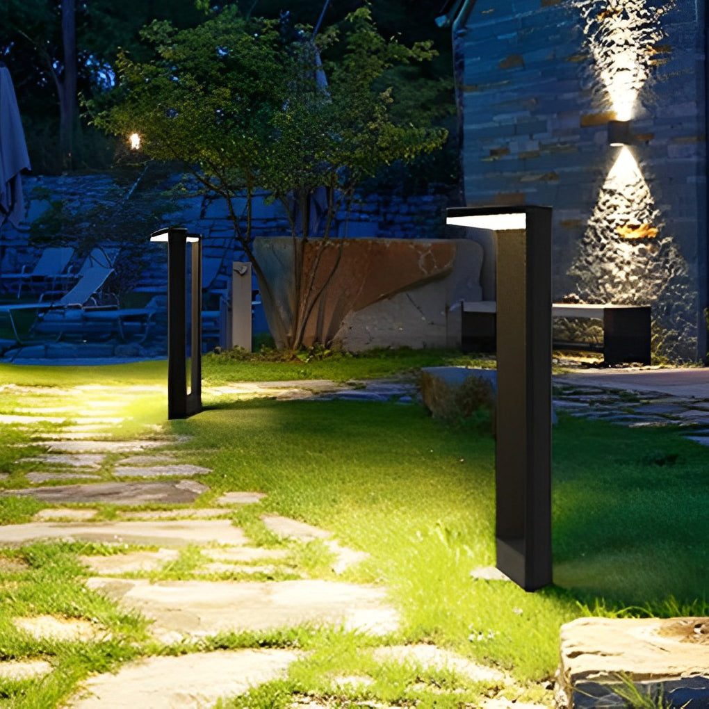 Tall architectural garden path lights glowing warmly on a green grass lawn near a stone wall.