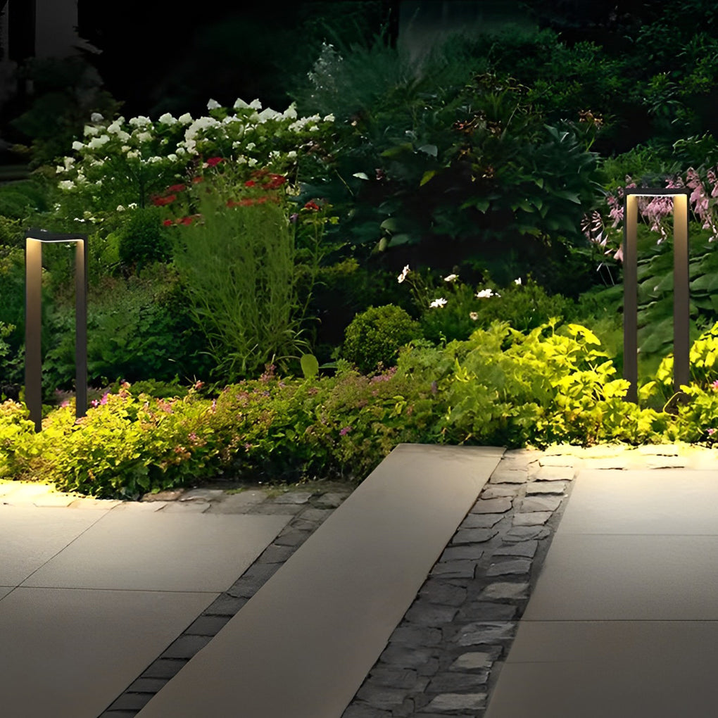 Tall architectural garden path lights glowing next to a paved stone walkway and lush greenery.