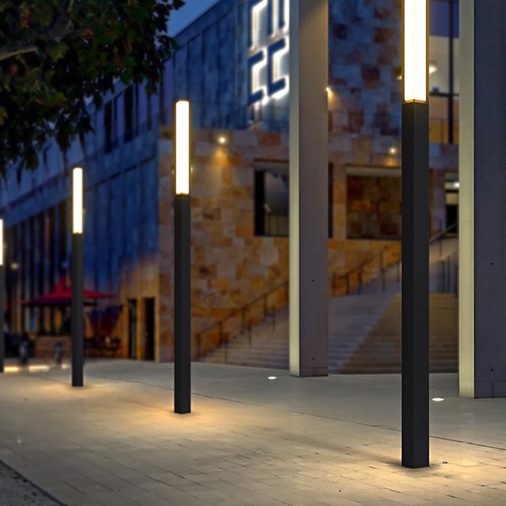 Tall black outdoor bollard lights illuminating a stone paved plaza path in front of a building.
