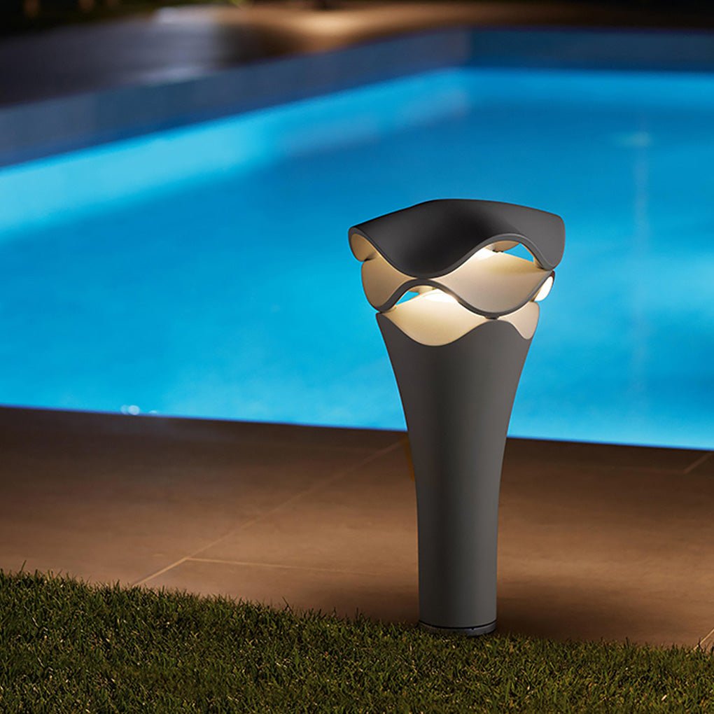 Tall wave design path light standing by a luxury blue swimming pool during a dark night scene.