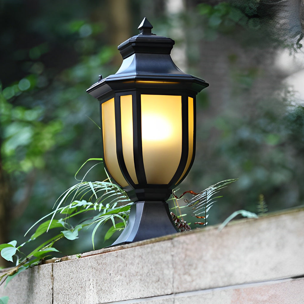 Traditional black vintage outdoor pillar lantern with warm light on a stone garden boundary.