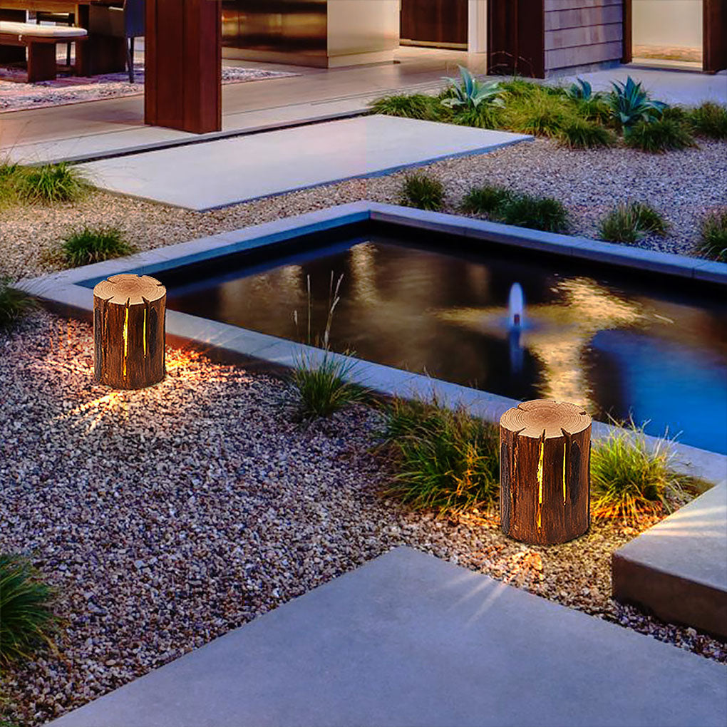 Tree stump lamp providing ambient illumination near a modern water feature.