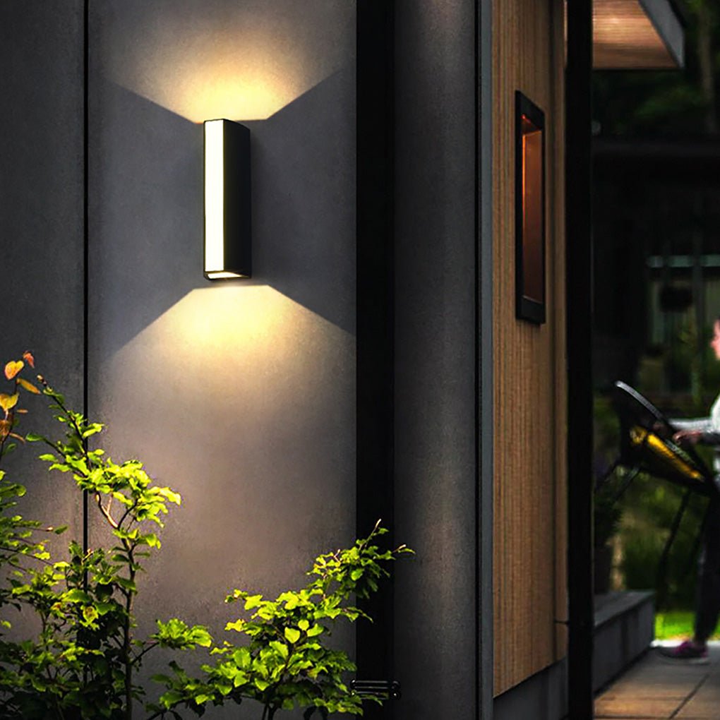 Up down cylinder sconce illuminating an exterior wall near plants, adding depth and atmosphere to a modern outdoor space.