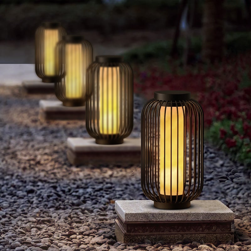 Lantern metal outdoor light with vertical design, placed on gravel pathway for warm and inviting garden lighting.