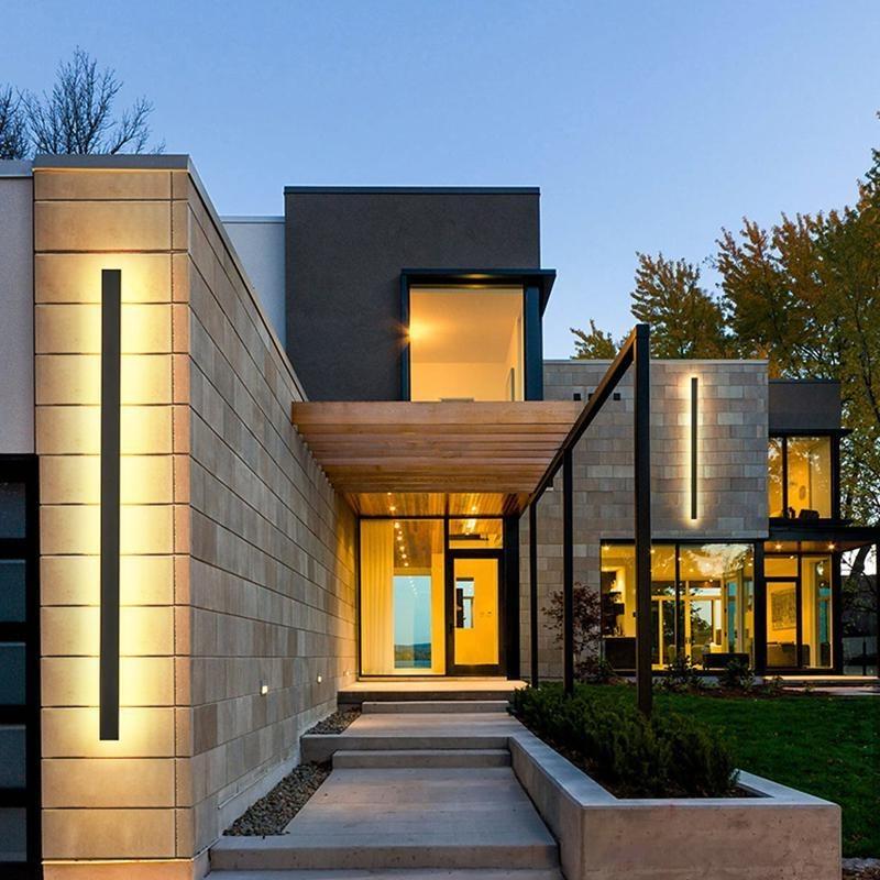 Long outdoor wall lights with vertical LED illumination, mounted on modern stone facade for sleek entrance lighting.
