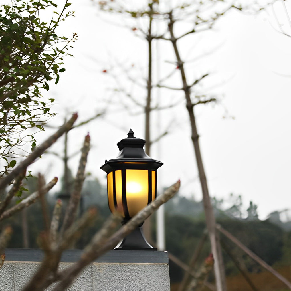 Vintage outdoor pillar lantern in black finish on a tall garden post under an overcast sky.