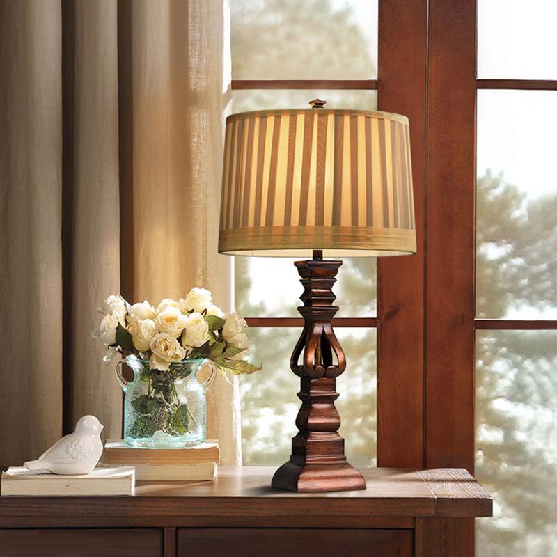 Vintage wood table lamp with a striped shade, placed beside a window with flowers.
