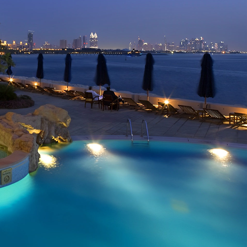 Waterproof outdoor spotlights illuminating a beachside pool with lounge chairs and city skyline view.