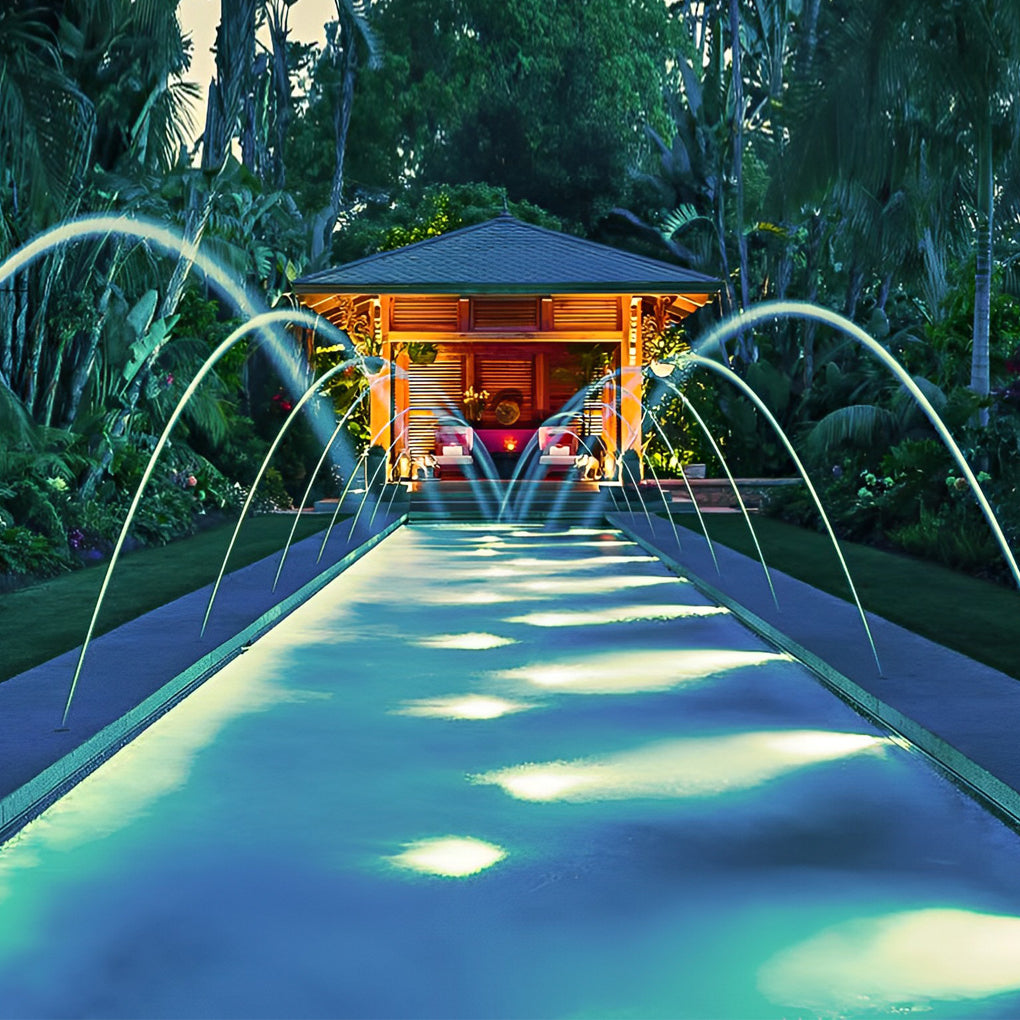 Waterproof outdoor spotlights lighting up a pathway with fountains and lush greenery in a garden.